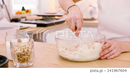 Cooking treat. Baker occupation. Woman hand kneading soft dough spoon in with preparing tasty home recipe pastry on table with peanut jar. 141967604