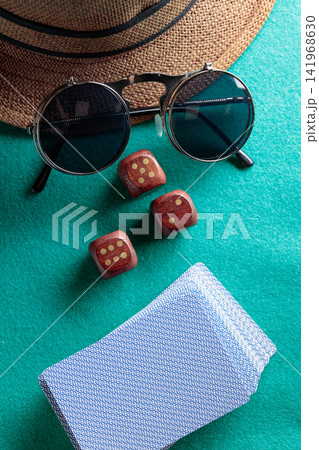 Playing cards, wooden dice, sunglasses and a hat on a green cloth. Playing cards, wooden dice, sunglasses and a hat on a green cloth. 141968630