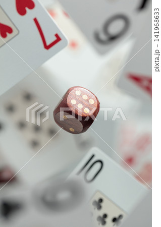 Wooden die in motion surrounded by playing cards. Wooden die in motion surrounded by playing cards. 141968633