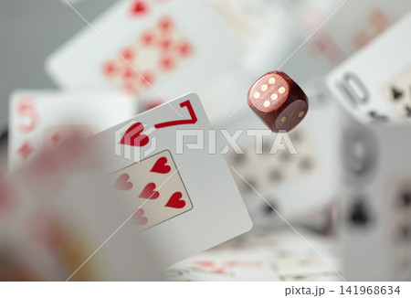 Wooden die in motion surrounded by playing cards. Wooden die in motion surrounded by playing cards. 141968634