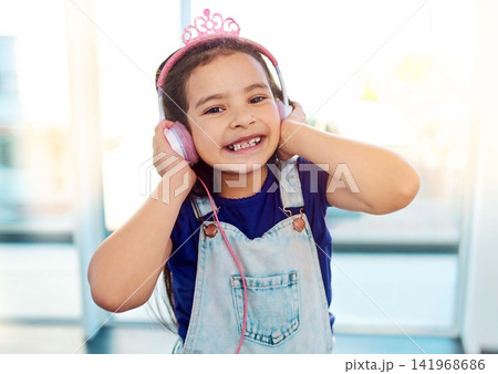 Young child, headphones and portrait for music listening in house with streaming song, radio sound and girl podcast. Happy, kid and earphones for media with smile, fun audio and playlist by window Young child, headphones and portrait for music listening in house with streaming song, radio sound and girl podcast. Happy, kid and earphones for media with smile, fun audio and playlist by window 141968686
