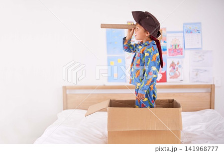 Child, box and pirate hat with spyglasses on bed in home for play, adventure and game as creativity. Boy, cardboard and tricorn with telescope in bedroom for fun, journey and activity as imagination Child, box and pirate hat with spyglasses on bed in home for play, adventure and game as creativity. Boy, cardboard and tricorn with telescope in bedroom for fun, journey and activity as imagination 141968777