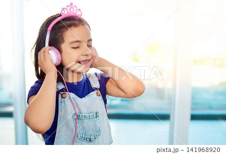 Young child, headphones and music listening in house with streaming song, radio sound and girl podcast. Happiness, kid and earphones for online media with smile, fun audio and playlist by home window Young child, headphones and music listening in house with streaming song, radio sound and girl podcast. Happiness, kid and earphones for online media with smile, fun audio and playlist by home window 141968920