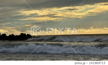 Ocean waves breaking near rocky breakwater at sunset under dramatic cloudy sky Ocean waves breaking near rocky breakwater at sunset under dramatic cloudy sky 141969713