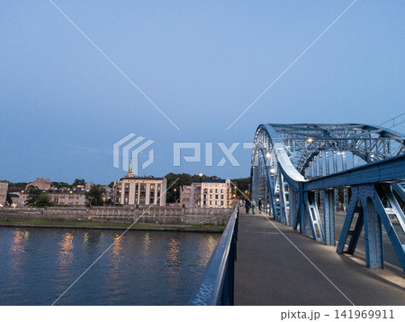 Grunwald Bridge over Vistula River in Krakow Poland at blue hour with illuminated steel arch bridge and riverside skyline Grunwald Bridge over Vistula River in Krakow Poland at blue hour with illuminated steel arch bridge and riverside skyline 141969911