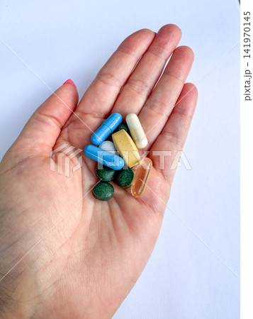 Assorted vitamins and supplements in a female hand, colorful capsules and tablets for health, pharmacy and wellness themes 141970145