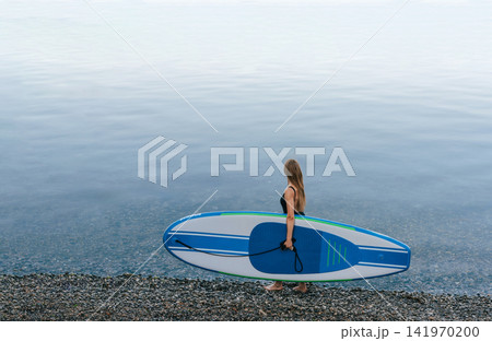 Woman Carrying Paddleboard to Calm Sea Woman Carrying Paddleboard to Calm Sea 141970200