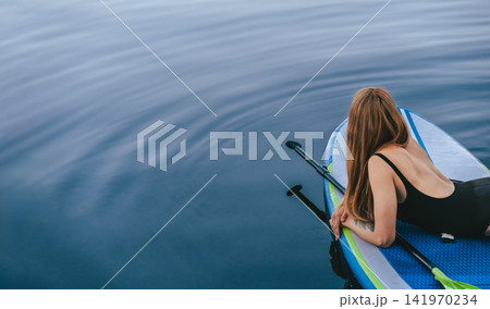 Woman Lying on Paddleboard Enjoying Slow Living Woman Lying on Paddleboard Enjoying Slow Living 141970234