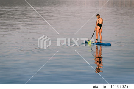 Woman Standing on Paddleboard Gliding over Sea 141970252