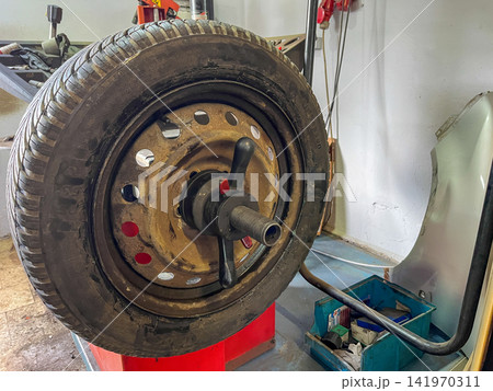 Used car wheel mounted on balancing machine in auto repair shop, ready for diagnostics, rotation or seasonal tire change 141970311