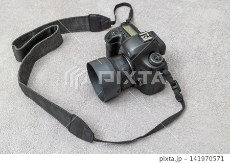 Black DSLR Camera with Lens Hood and Strap on Grey Surface Black DSLR Camera with Lens Hood and Strap on Grey Surface 141970571
