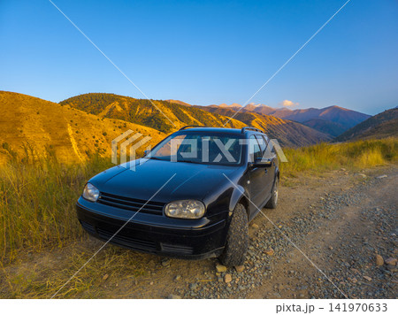 Black Station Wagon on Gravel Road in Mountain Landscape 141970633