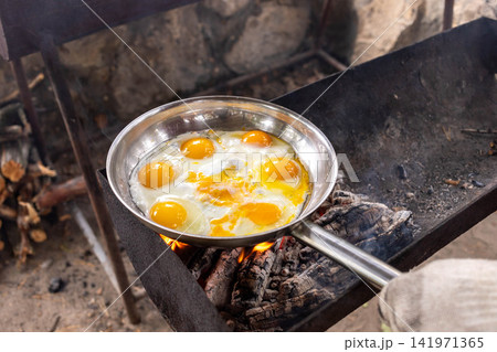 View to cooking eggs in a stainless steel pan over an open fire outdoors View to cooking eggs in a stainless steel pan over an open fire outdoors 141971365