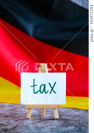 Paper note with words TAX on National symbol of Germany. German wave silky flag background. Tax planning system and economy policy  141971383