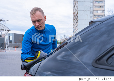 Concept of vehicle maintenance, wiping drying polishing car care cleanliness, modern contactless automated washing self services. Man cleans exterior of luxury car with microfiber rags. Automotive Concept of vehicle maintenance, wiping drying polishing car care cleanliness, modern contactless automated washing self services. Man cleans exterior of luxury car with microfiber rags. Automotive 141971427