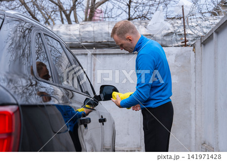 Concept of vehicle maintenance, wiping drying polishing car care cleanliness, modern contactless automated washing self services. Man cleans exterior of luxury car with microfiber rags. Automotive Concept of vehicle maintenance, wiping drying polishing car care cleanliness, modern contactless automated washing self services. Man cleans exterior of luxury car with microfiber rags. Automotive 141971428