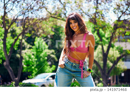 Beautiful, mature, Latina, Arab woman with dark hair, posing happily and inviting others to dance in an outdoor park. She's wearing a colorful retro pink outfit and jeans, and has makeup on. Beautiful, mature, Latina, Arab woman with dark hair, posing happily and inviting others to dance in an outdoor park. She's wearing a colorful retro pink outfit and jeans, and has makeup on. 141971468