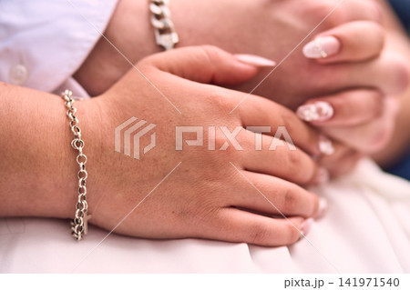 A view of a couple's hands, very affectionate, with details on the bride's nails, featuring figures and designs, their hands intertwined. Romance, engaged couple, union, love. A view of a couple's hands, very affectionate, with details on the bride's nails, featuring figures and designs, their hands intertwined. Romance, engaged couple, union, love. 141971540
