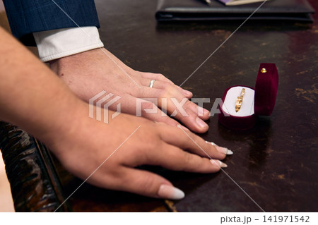 View of a couple's hands, placing their wedding rings on their fingers, in a civil ceremony; detail of their rings. Romance, bride and groom, union, love View of a couple's hands, placing their wedding rings on their fingers, in a civil ceremony; detail of their rings. Romance, bride and groom, union, love 141971542