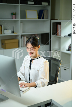 Smiling Young Asian Businesswoman Working at Computer Desk in Modern Office Smiling Young Asian Businesswoman Working at Computer Desk in Modern Office 141972311