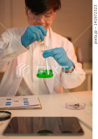 Scientist carefully mixes green solution in a flask 141972323