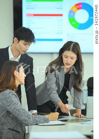 Three business professionals reviewing tablet data and reports during strategic meeting in modern office Three business professionals reviewing tablet data and reports during strategic meeting in modern office 141972440