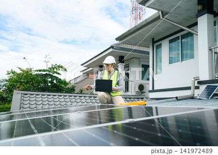 Asian Solar Engineer Inspecting Rooftop Solar Panels with Laptop on Residential House 141972489