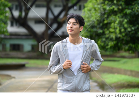 Young Asian Man Jogging in Park Wearing Sports Jacket Outdoors 141972537