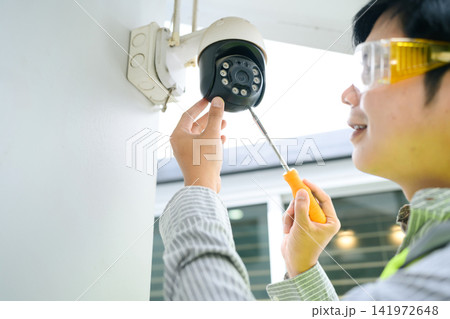 Technician Installing CCTV Security Camera on House Wall with Screwdriver 141972648