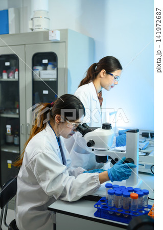 Two Female Scientists Working in Modern Research Laboratory with Microscope and Test Tubes Two Female Scientists Working in Modern Research Laboratory with Microscope and Test Tubes 141972687