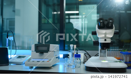 Modern Scientific Laboratory Workbench with Stereo Microscope, Analytical Balance, and Glassware in Blue-Tinted Research Facility 141972741