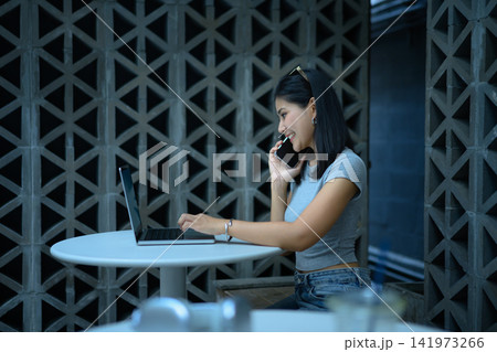 Young business woman working on a laptop and using smartphone sitting on at outdoor cafe workspace Young business woman working on a laptop and using smartphone sitting on at outdoor cafe workspace 141973266