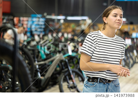 Interested young female shopper walking through bicycle shop Interested young female shopper walking through bicycle shop 141973988