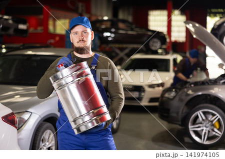 Positive male worker of car workshop holding metal fuel canister 141974105