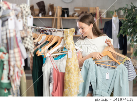 Positive teenage girl choosing something for summer in clothing store Positive teenage girl choosing something for summer in clothing store 141974119