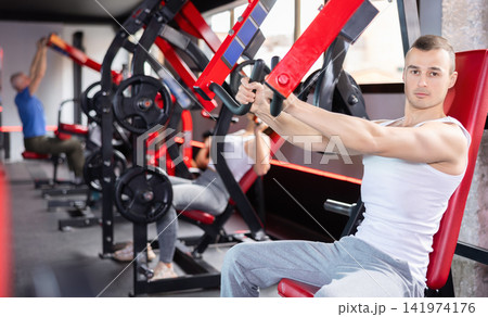 Young man trains his arms on machine Young man trains his arms on machine 141974176