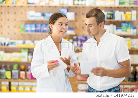 Female pharmacist consulting young guy about medicament according to recipe Female pharmacist consulting young guy about medicament according to recipe 141974215