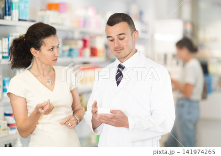 Male pharmacist consulting woman customer about medicament in box Male pharmacist consulting woman customer about medicament in box 141974265