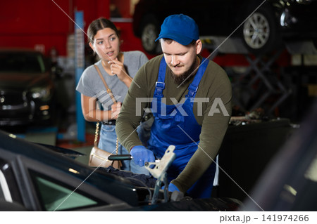 Skilled male auto mechanic controlling automobile detail while young girl looking at it disappointedly 141974266