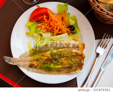 There is plate with fried solea flatfish and salad of fresh veg on wooden table. There is plate with fried solea flatfish and salad of fresh veg on wooden table. 141974301