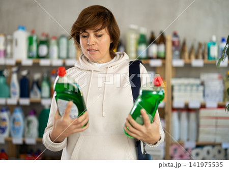 Adult woman chooses dishwashing detergent in store Adult woman chooses dishwashing detergent in store 141975535