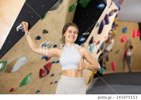 Cheerful girl giving thumbs up near bouldering wall in climbing gym 141975553