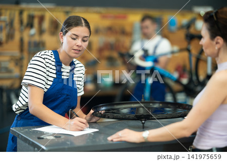 Young experienced girl seller taking order and talking with woman client about bicycle in workshop Young experienced girl seller taking order and talking with woman client about bicycle in workshop 141975659