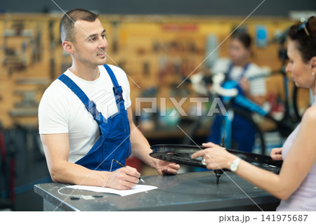 Young experienced man seller taking order and talking with woman client about bicycle in workshop Young experienced man seller taking order and talking with woman client about bicycle in workshop 141975687