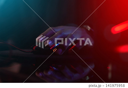 Hands, light and mouse for gaming, online and internet event with person at home in dark room. Influencer, gen z and gamer with playing for esports, video game and live streaming in bedroom in house Hands, light and mouse for gaming, online and internet event with person at home in dark room. Influencer, gen z and gamer with playing for esports, video game and live streaming in bedroom in house 141975958