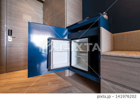 Hotel black minibar refrigerator guest room features a mini fridge neatly placed beneath a blue wooden desk, functional workspace with convenient in contemporary room. 141976202