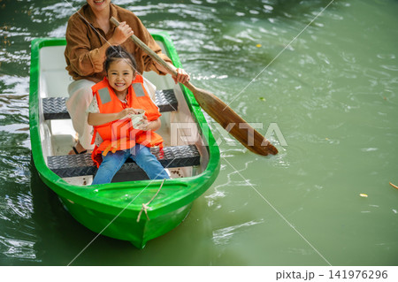mother and preschool child girl in a green paddle boat on a scenic pond. 141976296