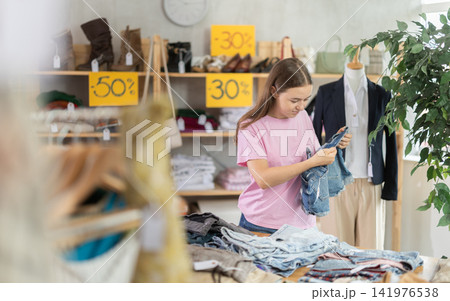 Teenage girl choosing jean shorts in clothing store Teenage girl choosing jean shorts in clothing store 141976538