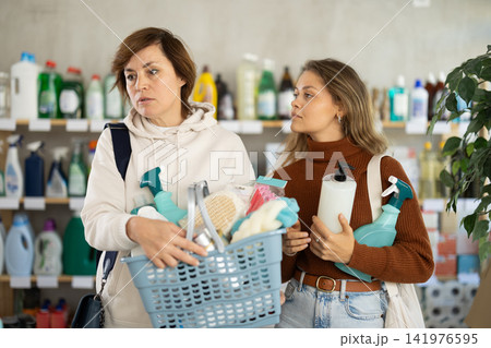 Two women with full basket choosing something in supermarket Two women with full basket choosing something in supermarket 141976595