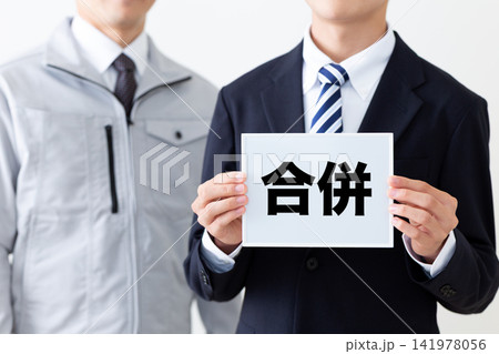 合併のホワイトボードを持つスーツを着た若い男性ビジネスマンと作業着のミドル男性 合併のホワイトボードを持つスーツを着た若い男性ビジネスマンと作業着のミドル男性 141978056